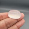 Macro photograph showing a monumental 75.44-carat natural Durr-e-Najaf (Clear Rock Crystal Quartz) cabochon resting on fingertips, featuring a large smooth oval dome, water-clear transparency, and subtle organic internal veil inclusions.