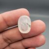 Macro photograph of a 14.40-carat natural Durr-e-Najaf (Clear Rock Crystal Quartz) cabochon held vertically in stainless steel gem tweezers, showcasing a high-domed oval cut, water-clear translucency, and soft internal feather inclusions.