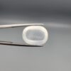 Macro photograph of a 14.05-carat natural Durr-e-Najaf (Clear Rock Crystal Quartz) cabochon held horizontally in stainless steel gem tweezers against a neutral grey background, displaying a smooth oval dome, water-clear transparency, and subtle organic internal veil inclusions.