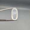 Macro photograph of a 12.09-carat natural Durr-e-Najaf (Clear Rock Crystal Quartz) cabochon held vertically in stainless steel gem tweezers against a neutral grey background, displaying an elongated oval polished dome, water-clear transparency, and subtle organic internal veil inclusions.