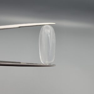 Multi-angle macro photographs of a 9.56-carat natural Durr-e-Najaf (Clear Rock Crystal Quartz) cabochon held vertically in stainless steel gem tweezers and resting on fingers, displaying an elegant slender elongated oval dome, water-clear transparency, and subtle organic internal veil growth.