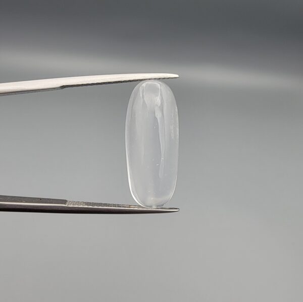 Multi-angle macro photographs of a 9.56-carat natural Durr-e-Najaf (Clear Rock Crystal Quartz) cabochon held vertically in stainless steel gem tweezers and resting on fingers, displaying an elegant slender elongated oval dome, water-clear transparency, and subtle organic internal veil growth.