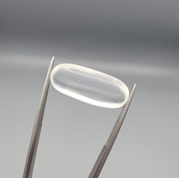 Multi-angle macro photographs of a 9.56-carat natural Durr-e-Najaf (Clear Rock Crystal Quartz) cabochon held vertically in stainless steel gem tweezers and resting on fingers, displaying an elegant slender elongated oval dome, water-clear transparency, and subtle organic internal veil growth.