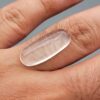 Multi-angle macro photographs of a 9.56-carat natural Durr-e-Najaf (Clear Rock Crystal Quartz) cabochon held vertically in stainless steel gem tweezers and resting on fingers, displaying an elegant slender elongated oval dome, water-clear transparency, and subtle organic internal veil growth.