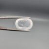 Macro photograph of an 11.36-carat natural Durr-e-Najaf (Clear Rock Crystal Quartz) cabochon held horizontally in stainless steel gem tweezers against a neutral grey background, displaying a smooth oval dome, water-clear transparency, and subtle organic internal veil inclusions.