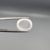 Macro photograph of a 10.46-carat natural Durr-e-Najaf (Clear Rock Crystal Quartz) cabochon held horizontally in stainless steel gem tweezers against a neutral grey background, displaying a smooth oval dome, water-clear transparency, and subtle organic internal veil inclusions.