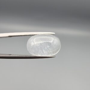 Macro photograph of a 9.24-carat natural Durr-e-Najaf (Clear Rock Crystal Quartz) cabochon held horizontally in stainless steel gem tweezers against a neutral grey background, displaying a smooth oval dome, water-clear transparency, and subtle organic internal veil inclusions.