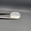 Macro photograph of a 9.24-carat natural Durr-e-Najaf (Clear Rock Crystal Quartz) cabochon held horizontally in stainless steel gem tweezers against a neutral grey background, displaying a smooth oval dome, water-clear transparency, and subtle organic internal veil inclusions.