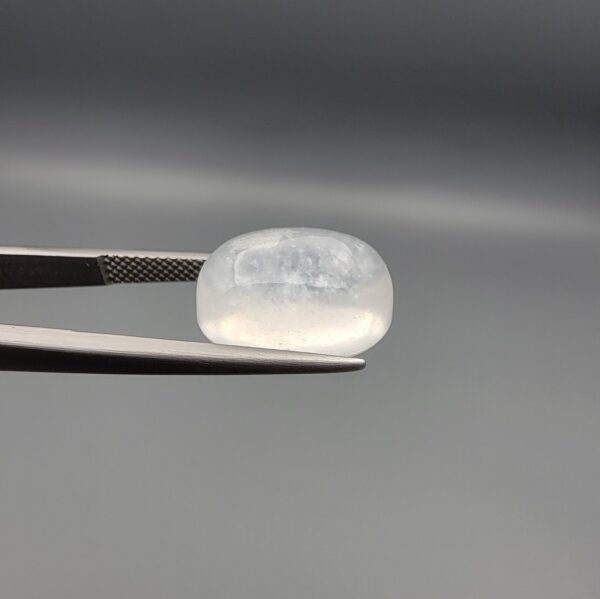 Macro photograph of a 9.24-carat natural Durr-e-Najaf (Clear Rock Crystal Quartz) cabochon held horizontally in stainless steel gem tweezers against a neutral grey background, displaying a smooth oval dome, water-clear transparency, and subtle organic internal veil inclusions.