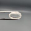 Macro photograph of an 11.47-carat natural Durr-e-Najaf (Clear Rock Crystal Quartz) cabochon held horizontally in stainless steel gem tweezers against a neutral grey background, displaying a smooth oval dome, water-clear transparency, and subtle organic internal veil inclusions.
