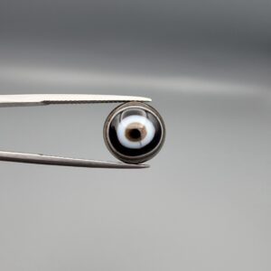 Multi-angle macro photographs of a 5.87-carat natural African Black Eye Agate (Sulemani Aqeeq) held in steel gem tweezers, showcasing a high round cabochon dome with concentric black and stark white banding, a brownish-black core pupil, and a base revealing dendritic veins.