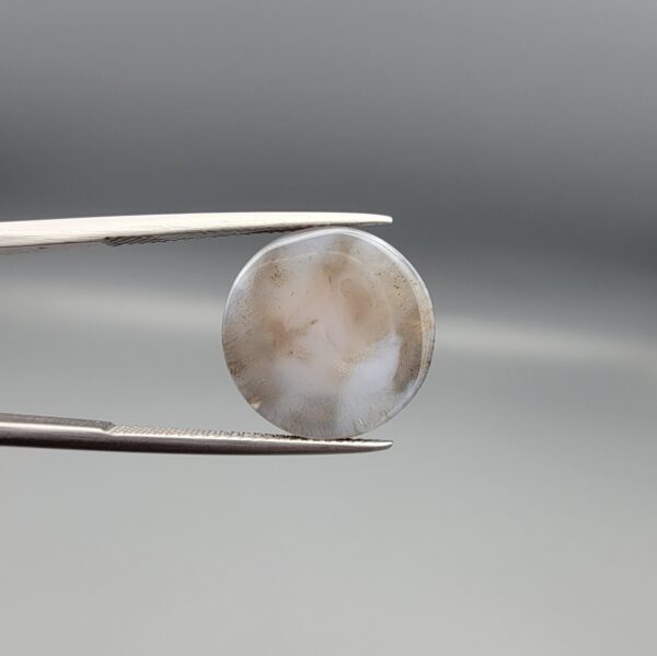 Multi-angle macro photographs of a 12.93-carat natural African Black Eye Agate (Sulemani Aqeeq) held in gem tweezers, showcasing a high round cabochon dome with sharp concentric white and brown banding, a dark brown core pupil, and a base showing natural chalcedony matrix patterns.