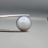 Multi-angle macro photographs of a 12.06-carat natural African Eye Agate (Sulemani Aqeeq) held in gem tweezers, showing a high round cabochon dome with translucent white and grey halo banding, a luminous bright focal center, and a base with natural black mineral plume inclusions.