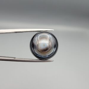 Multi-angle macro photographs of a 12.60-carat natural African Eye Agate (Sulemani Aqeeq) held in gem tweezers, showcasing a high round cabochon dome with concentric white, grey, and jet-black banding, a brownish-grey core pupil, and a polished black base with a subtle light halo center.