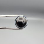 Multi-angle macro photographs of a 14.77-carat natural African Eye Agate (Sulemani Aqeeq) held in gem tweezers, showing a high round cabochon dome with a deep onyx-black core, sharp white outer ringing, tiered side profile bands, and a flat jet-black base with fine white agate pinstripes.