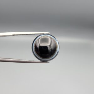 Multi-angle macro photographs of a 14.77-carat natural African Eye Agate (Sulemani Aqeeq) held in gem tweezers, showing a high round cabochon dome with a deep onyx-black core, sharp white outer ringing, tiered side profile bands, and a flat jet-black base with fine white agate pinstripes.