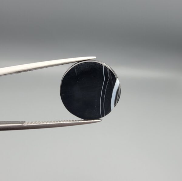 Multi-angle macro photographs of a 14.77-carat natural African Eye Agate (Sulemani Aqeeq) held in gem tweezers, showing a high round cabochon dome with a deep onyx-black core, sharp white outer ringing, tiered side profile bands, and a flat jet-black base with fine white agate pinstripes.