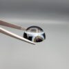 Multi-angle macro photographs of a 14.77-carat natural African Eye Agate (Sulemani Aqeeq) held in gem tweezers, showing a high round cabochon dome with a deep onyx-black core, sharp white outer ringing, tiered side profile bands, and a flat jet-black base with fine white agate pinstripes.