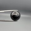 Multi-angle macro photographs of a 12.99-carat natural African Eye Agate (Sulemani Aqeeq) held in gem tweezers, showcasing a high round cabochon dome with deep charcoal-black body color, subtle flank fortification banding, and a base filled with intricate dendritic mineral inclusions.