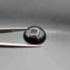 Multi-angle macro photographs of a 12.99-carat natural African Eye Agate (Sulemani Aqeeq) held in gem tweezers, showcasing a high round cabochon dome with deep charcoal-black body color, subtle flank fortification banding, and a base filled with intricate dendritic mineral inclusions.
