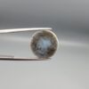 Multi-angle macro photographs of a 12.99-carat natural African Eye Agate (Sulemani Aqeeq) held in gem tweezers, showcasing a high round cabochon dome with deep charcoal-black body color, subtle flank fortification banding, and a base filled with intricate dendritic mineral inclusions.