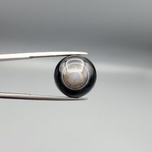 Multi-angle macro photographs of a 13.29-carat natural African Banded Eye Agate (Sulemani Aqeeq) held in gem tweezers, displaying a high round cabochon dome with concentric white and grey ringing around a translucent light core, a black border, and a reverse side showing undulating blue-grey wave banding.