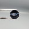 Multi-angle macro photographs of a 13.29-carat natural African Banded Eye Agate (Sulemani Aqeeq) held in gem tweezers, displaying a high round cabochon dome with concentric white and grey ringing around a translucent light core, a black border, and a reverse side showing undulating blue-grey wave banding.