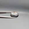 Multi-angle macro photographs of a 12.87-carat natural African Banded Eye Agate (Sulemani Aqeeq) held in gem tweezers, displaying a high round cabochon dome with concentric white and grey fortification rings, a brownish-black core pupil, and a base showing soft blue-grey to dark gradient chalcedony.