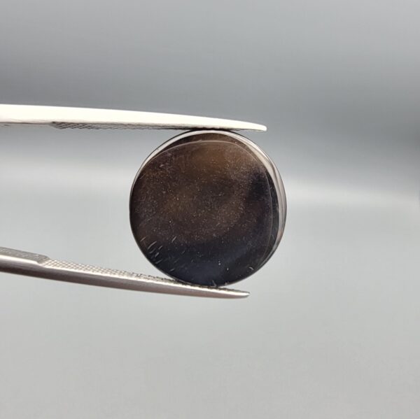 Multi-angle macro photographs of a 12.76-carat natural African Banded Eye Agate (Sulemani Aqeeq) held in gem tweezers, displaying a high round cabochon dome with concentric white and dark brown fortification rings framing a defined eye motif, tiered side profile banding, and a smooth dark brown base.