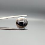 Multi-angle macro photographs of an 8.02-carat natural African Banded Eye Agate (Sulemani Aqeeq) held in steel gem tweezers, displaying a high round cabochon dome with wavy concentric white and earth-brown banding around a deep black core, crisp side fortification layers, and a flat jet-black base.