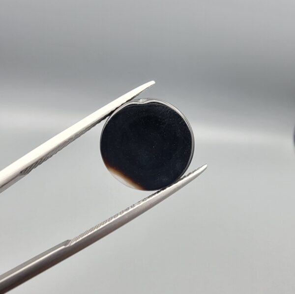 Multi-angle macro photographs of an 8.02-carat natural African Banded Eye Agate (Sulemani Aqeeq) held in steel gem tweezers, displaying a high round cabochon dome with wavy concentric white and earth-brown banding around a deep black core, crisp side fortification layers, and a flat jet-black base.