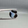 Multi-angle macro photographs of a 5.64-carat natural African Banded Eye Agate (Sulemani Aqeeq) held in gem tweezers, displaying a high round cabochon dome with precise concentric white and warm brown fortification rings around a dark brown core, crisp side profile banding, and a reverse side showing a unique tricolor blue, white, and dark brown pattern.