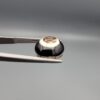 Multi-angle macro photographs of a 5.62-carat natural African Banded Eye Agate (Sulemani Aqeeq) held in steel gem tweezers, showcasing a high round cabochon dome with bold concentric white and jet-black banding framing a brownish-black pupil core, crisp side profile layers, and a flat white base with natural dark dendrite plumes.