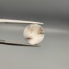 Multi-angle macro photographs of a 5.62-carat natural African Banded Eye Agate (Sulemani Aqeeq) held in steel gem tweezers, showcasing a high round cabochon dome with bold concentric white and jet-black banding framing a brownish-black pupil core, crisp side profile layers, and a flat white base with natural dark dendrite plumes.