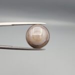 Multi-angle macro photographs of a 10.43-carat natural African Banded Eye Agate (Sulemani Aqeeq) held in gem tweezers, displaying a high round cabochon dome with translucent smoky-white mist halo eye banding, flank-textured fortification rings along the side profile, and a flat translucent base with a bright focal spot center.