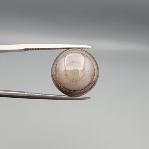 Multi-angle macro photographs of a 10.43-carat natural African Banded Eye Agate (Sulemani Aqeeq) held in gem tweezers, displaying a high round cabochon dome with translucent smoky-white mist halo eye banding, flank-textured fortification rings along the side profile, and a flat translucent base with a bright focal spot center.