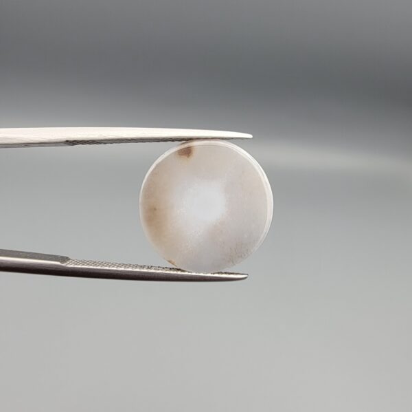 Multi-angle macro photographs of a 10.43-carat natural African Banded Eye Agate (Sulemani Aqeeq) held in gem tweezers, displaying a high round cabochon dome with translucent smoky-white mist halo eye banding, flank-textured fortification rings along the side profile, and a flat translucent base with a bright focal spot center.
