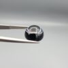 Multi-angle macro photographs of a 6.67-carat natural African Banded Eye Agate (Sulemani Aqeeq) held in gem tweezers, showing a high round cabochon dome with a deep onyx-black body framed by a sharp, concentric white outer arc, smooth profile curvature, and a polished solid black reverse base.