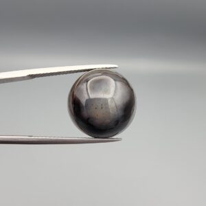 Multi-angle macro photographs of a 13.29-carat natural African Banded Eye Agate (Sulemani Aqeeq) shown in gem tweezers and held on a finger, featuring a high round cabochon dome with a deep charcoal body, subtle translucent inner zoning, layered side fortification bands, and a smooth black base.