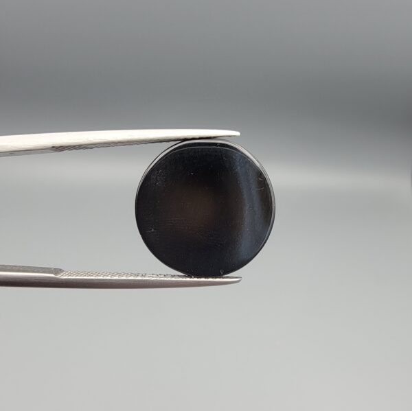 Multi-angle macro photographs of a 13.29-carat natural African Banded Eye Agate (Sulemani Aqeeq) shown in gem tweezers and held on a finger, featuring a high round cabochon dome with a deep charcoal body, subtle translucent inner zoning, layered side fortification bands, and a smooth black base.