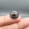 Multi-angle macro photographs of a 13.29-carat natural African Banded Eye Agate (Sulemani Aqeeq) shown in gem tweezers and held on a finger, featuring a high round cabochon dome with a deep charcoal body, subtle translucent inner zoning, layered side fortification bands, and a smooth black base.