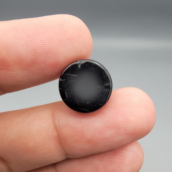 Multi-angle macro photographs of a 14.55-carat natural African Banded Eye Agate (Sulemani Aqeeq) held on fingers, showcasing a high round cabochon dome with sharp concentric white and black fortification rings framing a deep black pupil core, and a smooth jet-black base.