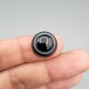 Multi-angle macro photographs of a 14.09-carat natural African Banded Eye Agate (Sulemani Aqeeq) held on fingertips, displaying a high round cabochon dome with a deep onyx-black core framed by sharp concentric white outer ringing, layered side profile banding, and a smooth jet-black reverse base.