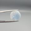 Multi-angle macro photographs of a 10.42-carat natural African Banded Eye Agate (Sulemani Aqeeq) held in tweezers and on fingertips, displaying a high round cabochon dome with a luminous translucent ice-blue eye core framed by dark fortification rings, layered side flank banding, and a webbed blue-grey chalcedony base.