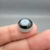 Multi-angle macro photographs of a 10.42-carat natural African Banded Eye Agate (Sulemani Aqeeq) held in tweezers and on fingertips, displaying a high round cabochon dome with a luminous translucent ice-blue eye core framed by dark fortification rings, layered side flank banding, and a webbed blue-grey chalcedony base.