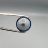 Multi-angle macro photographs of a 13.83-carat natural African Banded Eye Agate (Sulemani Aqeeq) held in steel gem tweezers, showcasing a high round cabochon dome with a luminous translucent ice-blue central eye field, framed by a deep black margin, and a smooth jet-black flat reverse base.