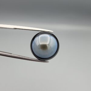 Multi-angle macro photographs of a 13.83-carat natural African Banded Eye Agate (Sulemani Aqeeq) held in steel gem tweezers, showcasing a high round cabochon dome with a luminous translucent ice-blue central eye field, framed by a deep black margin, and a smooth jet-black flat reverse base.
