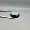 Multi-angle macro photographs of a 13.83-carat natural African Banded Eye Agate (Sulemani Aqeeq) held in steel gem tweezers, showcasing a high round cabochon dome with a luminous translucent ice-blue central eye field, framed by a deep black margin, and a smooth jet-black flat reverse base.
