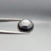 Multi-angle macro photographs of a 10.47-carat natural African Banded Eye Agate (Sulemani Aqeeq) shown in gem tweezers and on fingertips, featuring a high round cabochon dome with concentric black, brown, and white fortification rings framing a luminous pale blue-grey eye core, parallel layered profile banding, and a dark mottled reverse base with a nebulous center.