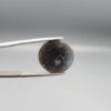 Multi-angle macro photographs of a 10.47-carat natural African Banded Eye Agate (Sulemani Aqeeq) shown in gem tweezers and on fingertips, featuring a high round cabochon dome with concentric black, brown, and white fortification rings framing a luminous pale blue-grey eye core, parallel layered profile banding, and a dark mottled reverse base with a nebulous center.
